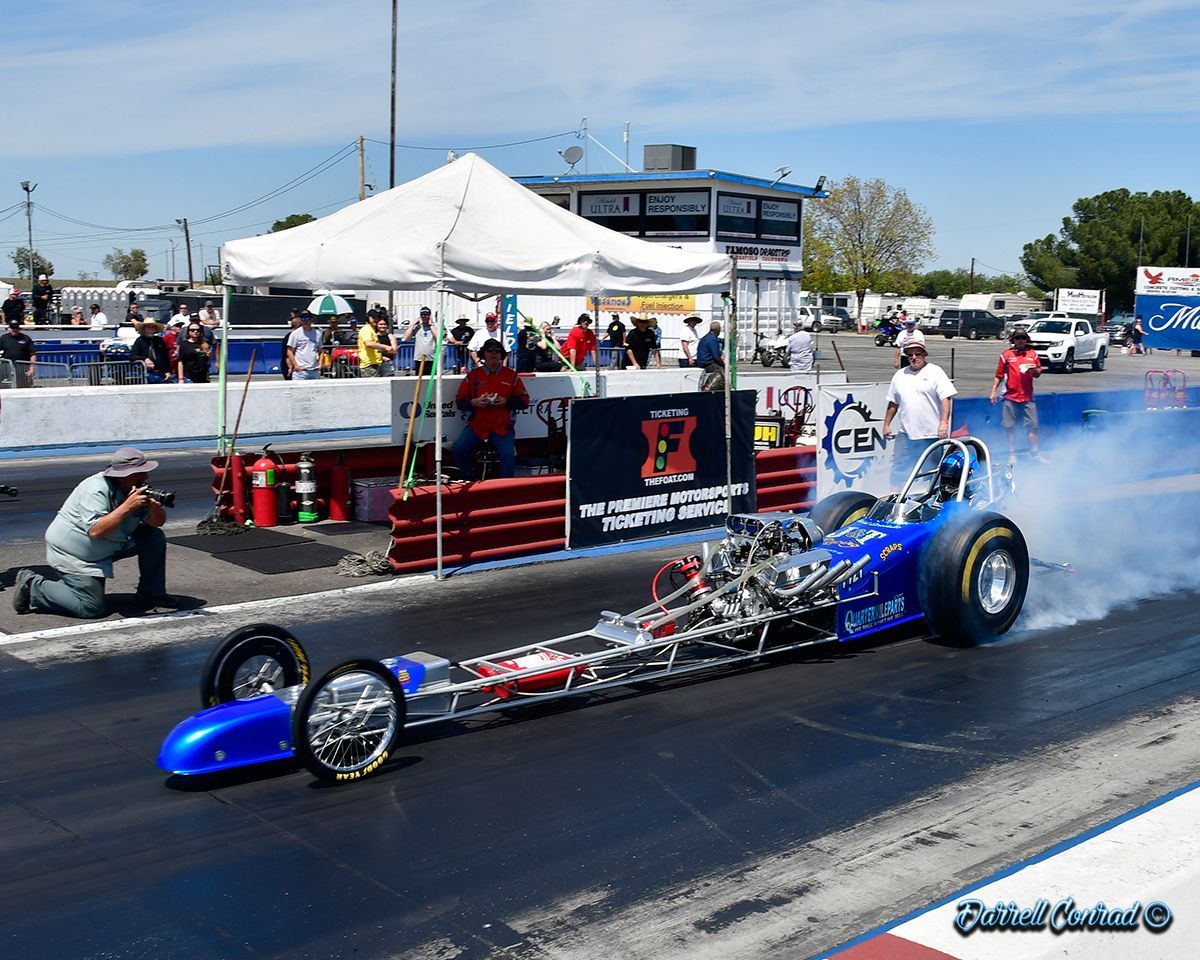 A blue dragster is driving down a race track