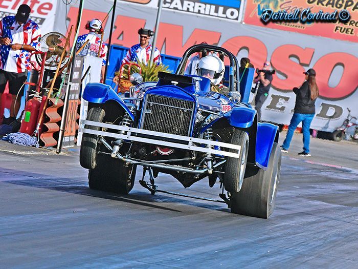 A blue car is driving down a race track in front of a sign that says carrillo