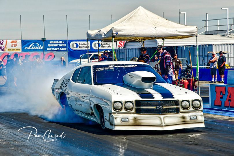 A white and blue race car is doing a burnout on a race track.