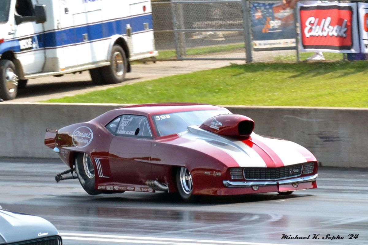 A red and white racing car is on a track with an ambulance in the background