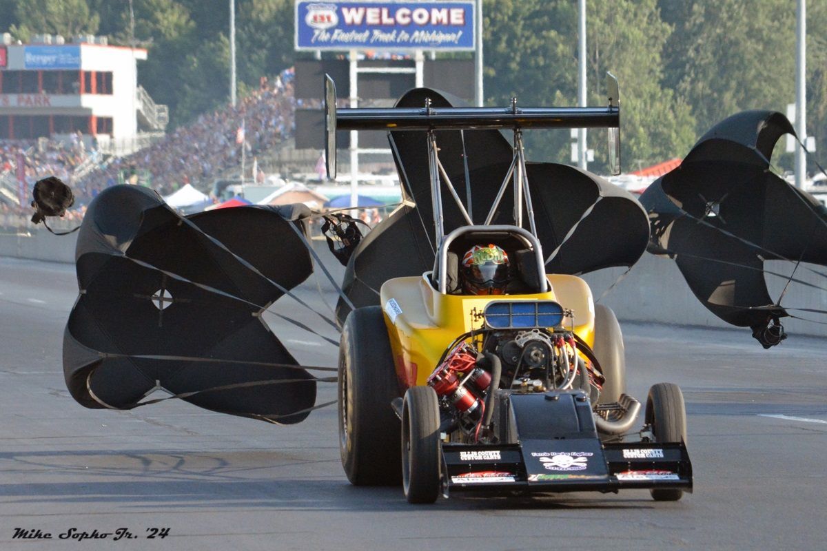 A yellow race car with a welcome sign in the background