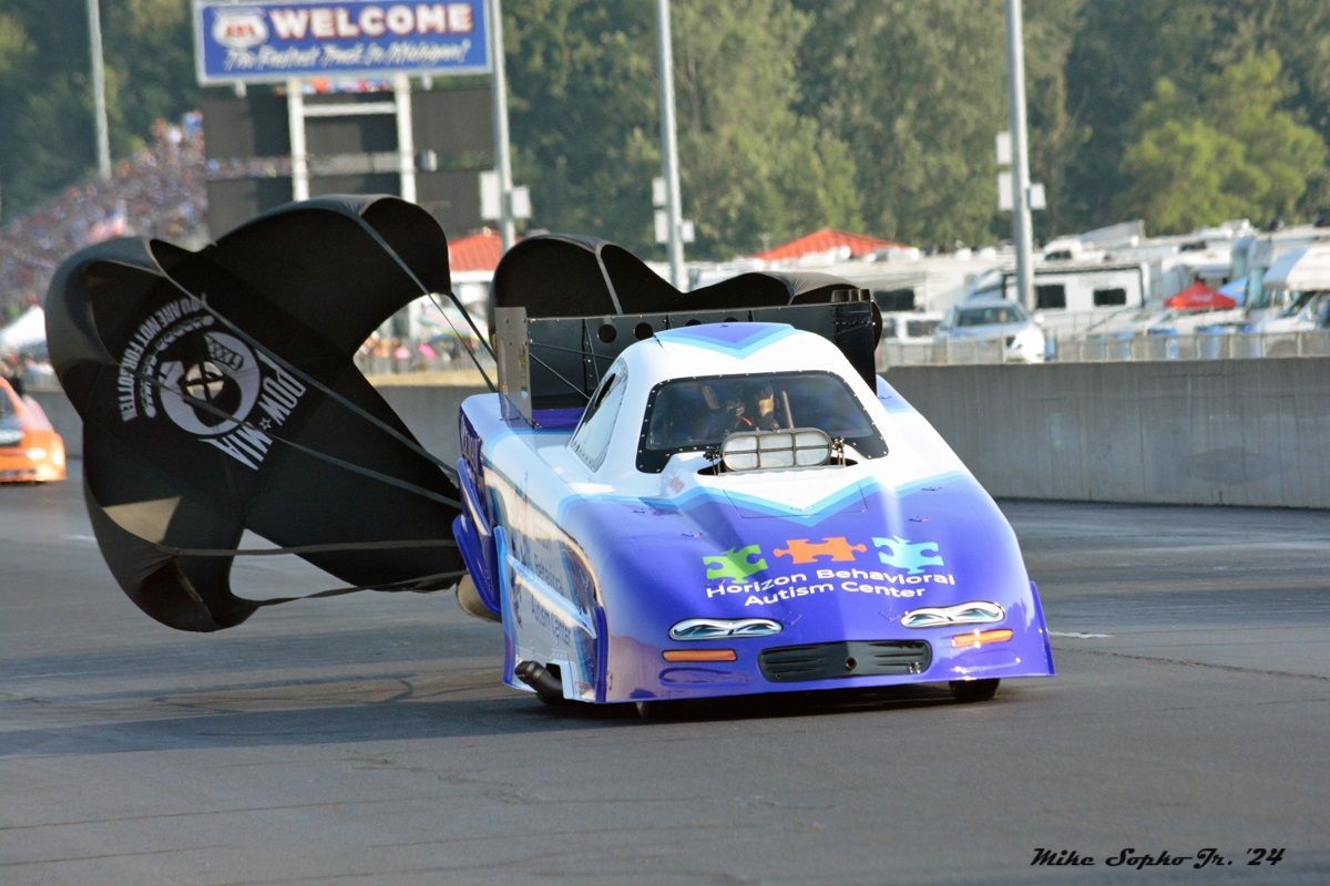 A blue and white race car with a welcome sign in the background
