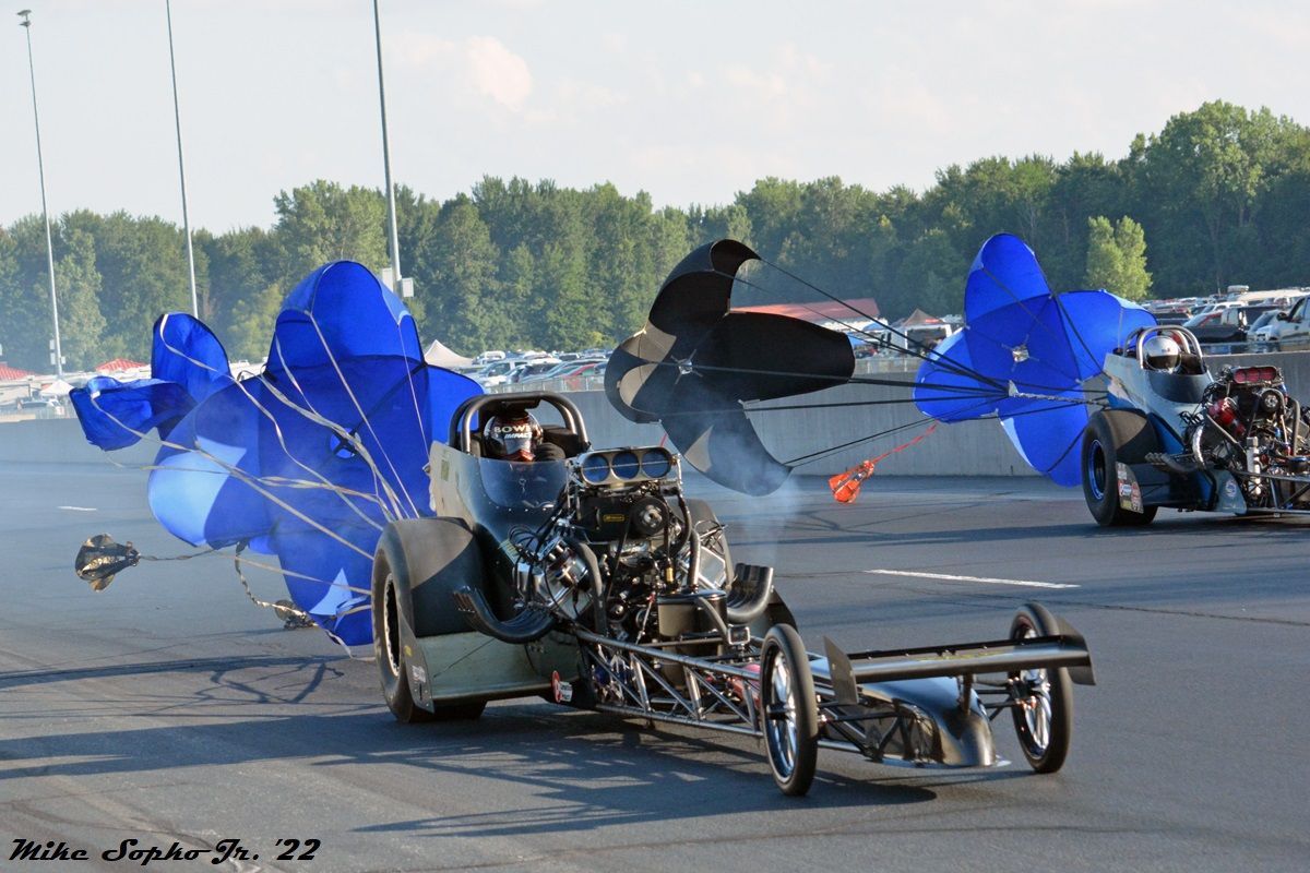 Two drag racing cars are racing on a track with blue smoke coming out of their engines