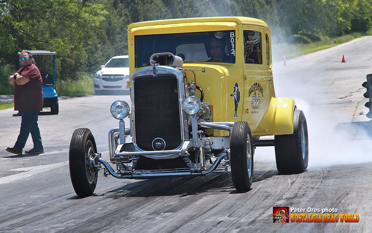 A yellow car is driving down a road with smoke coming out of the tires