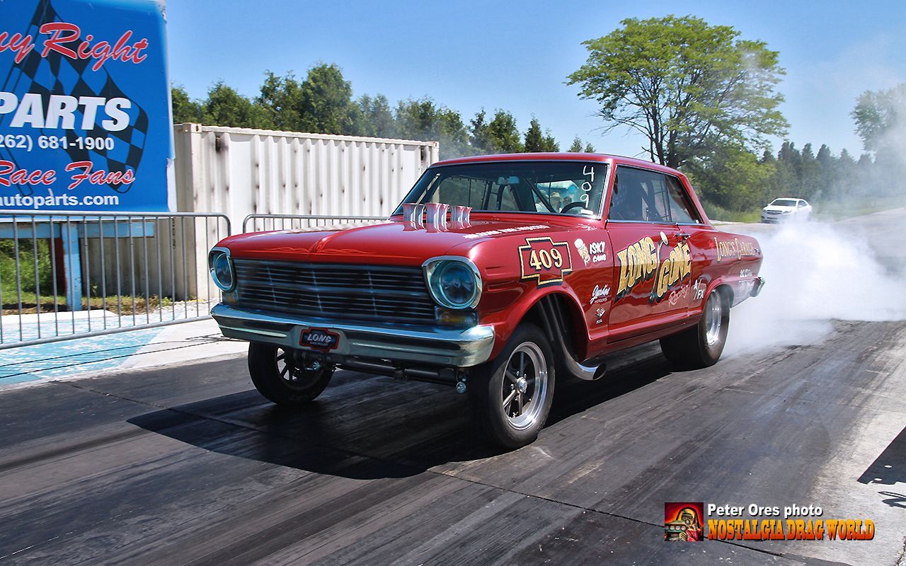 A red car is driving down a race track in front of a sign that says parts