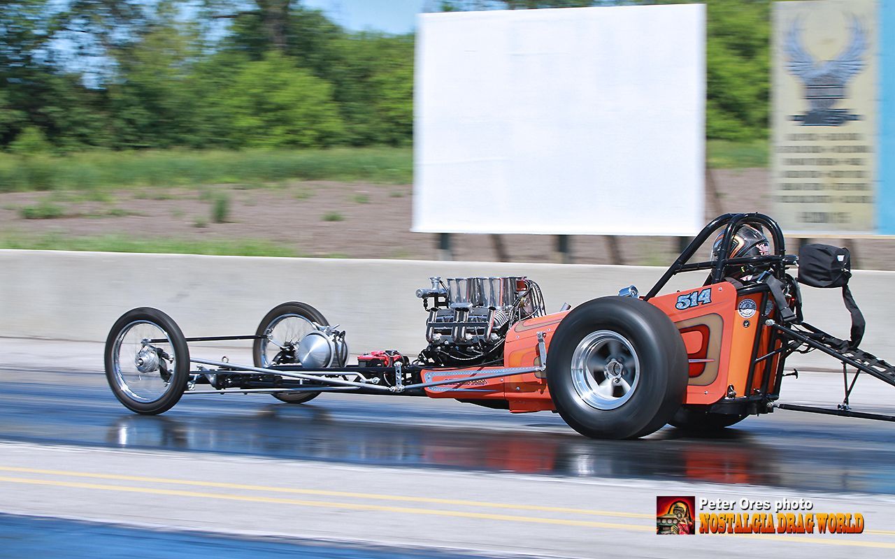 A dragster is driving down a track with a white sign in the background.