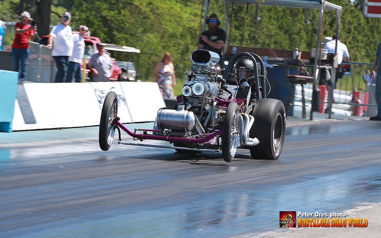 A dragster is driving down a race track with people watching.