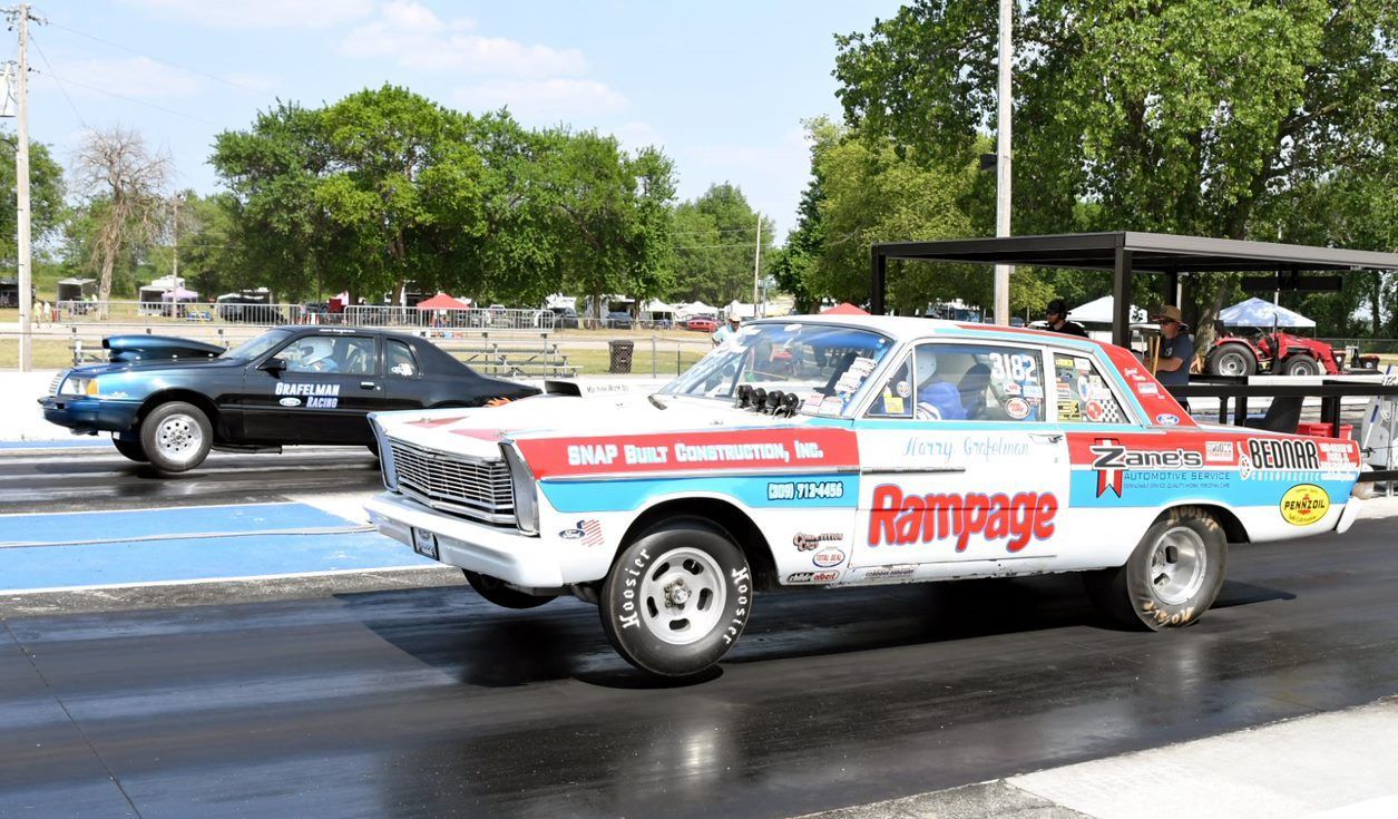 A race car is driving down a track next to a black car.