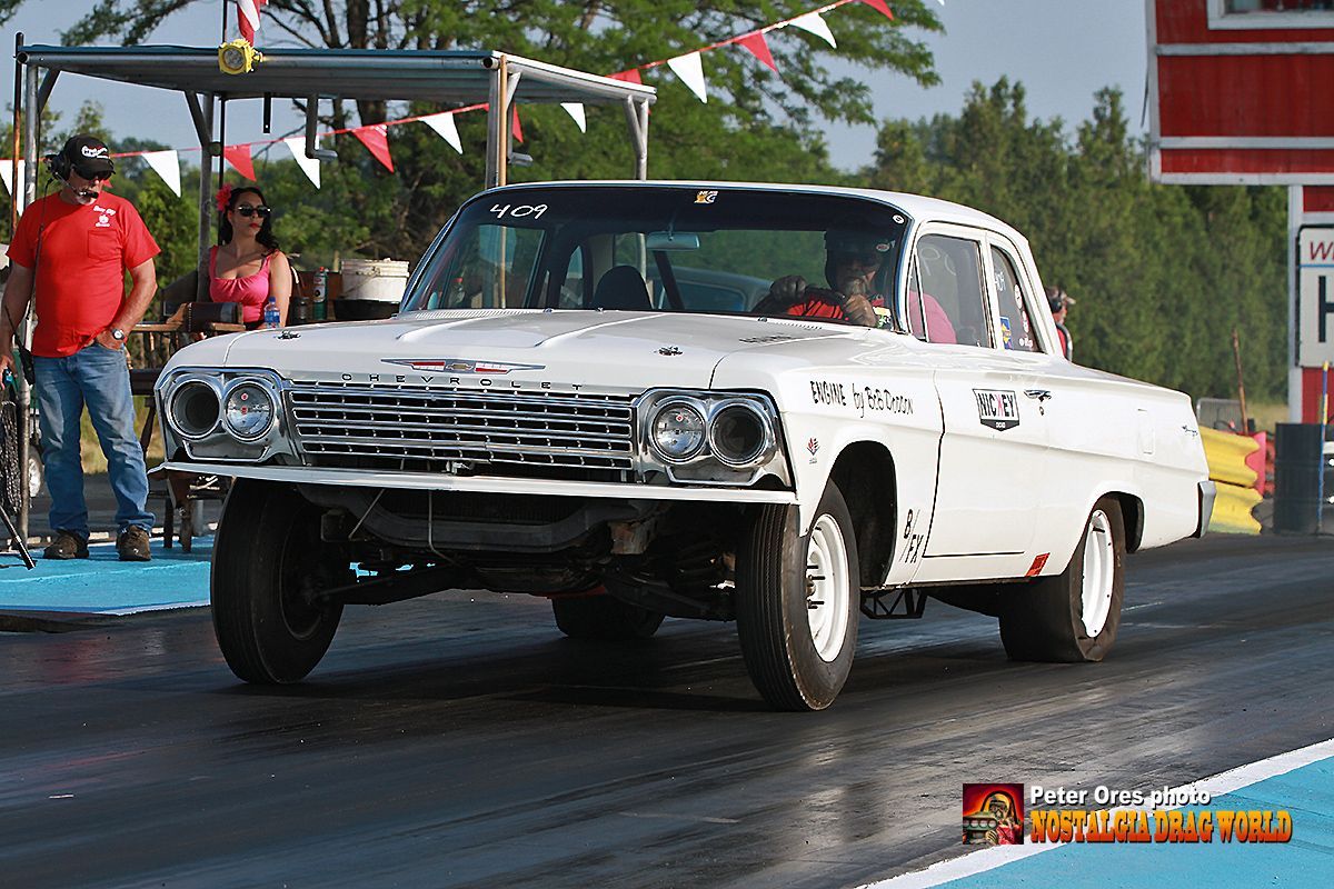 A white car is on a race track with a man in a red shirt standing behind it