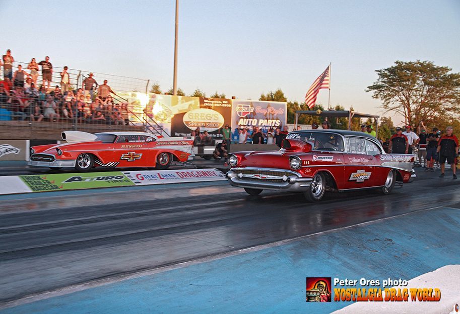 Two old cars are racing on a race track.