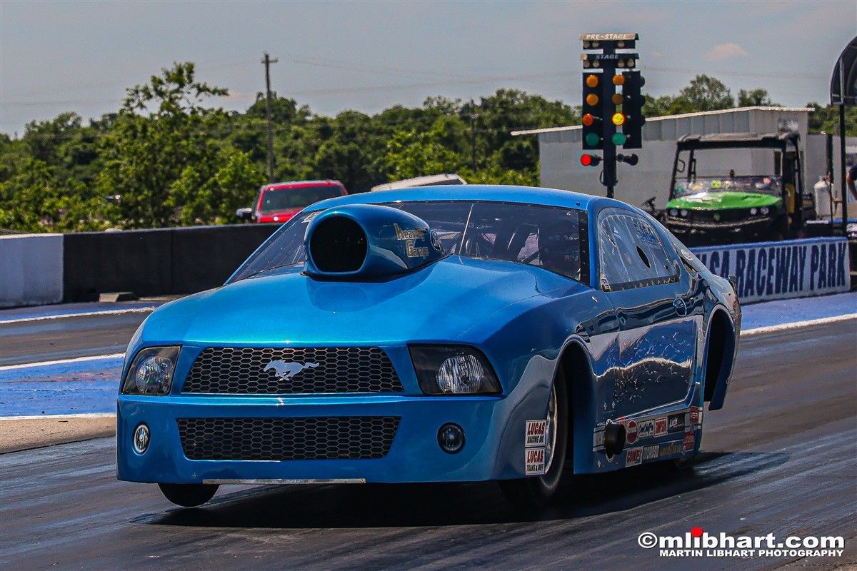 A blue ford mustang is driving down a race track