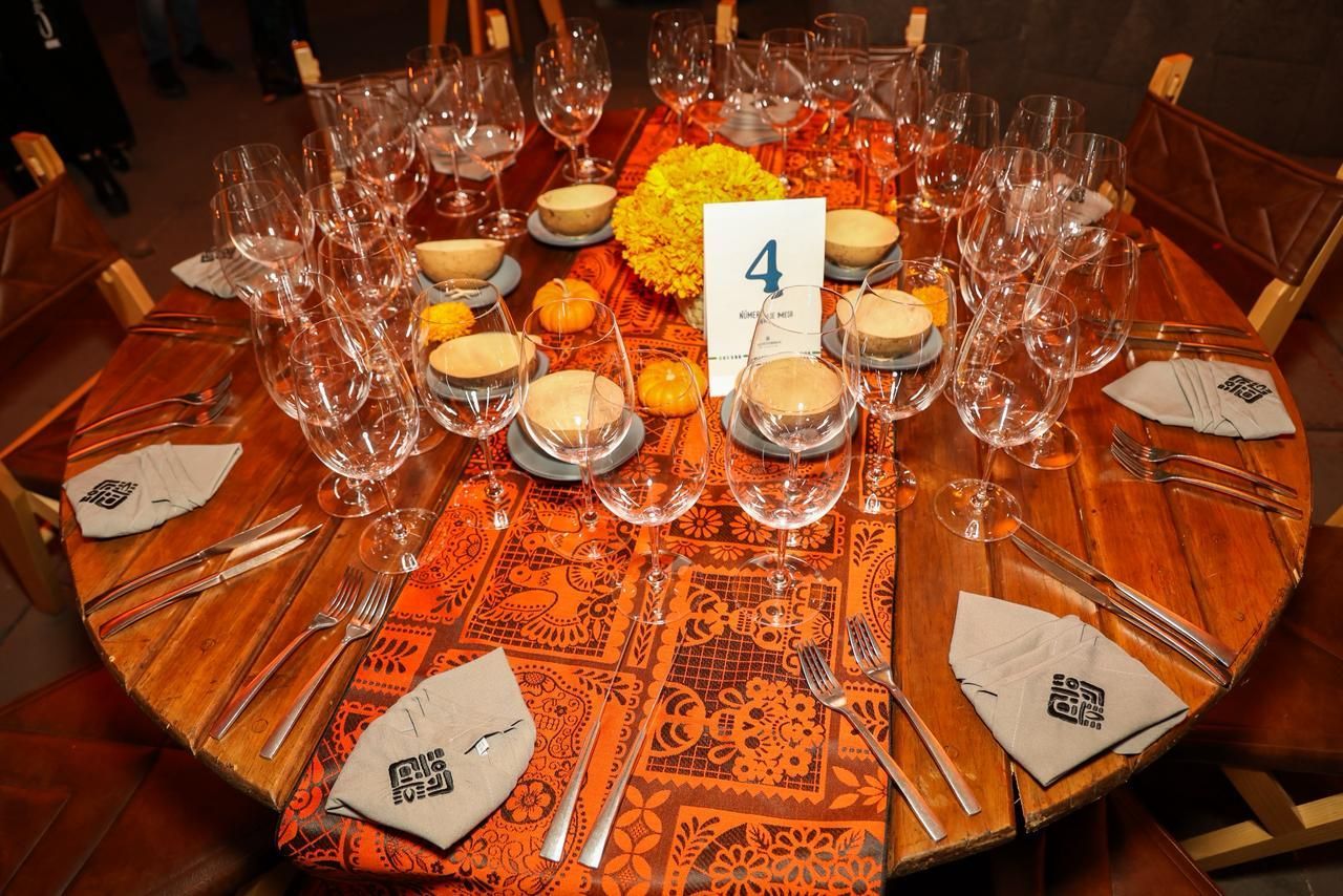Juego de mesa redonda de madera para cena con centro de mesa y cubiertos florales de color naranja.
