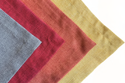 Cuatro muestras de tela dispuestas en patrón de chevron, en transición de gris a rojo, naranja y dorado.