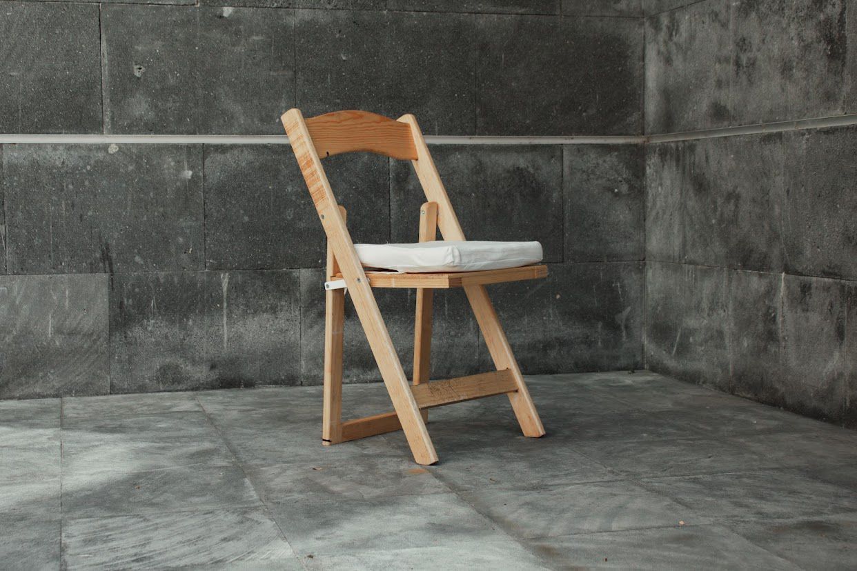 Silla plegable de madera con cojín blanco en una habitación de paredes grises.