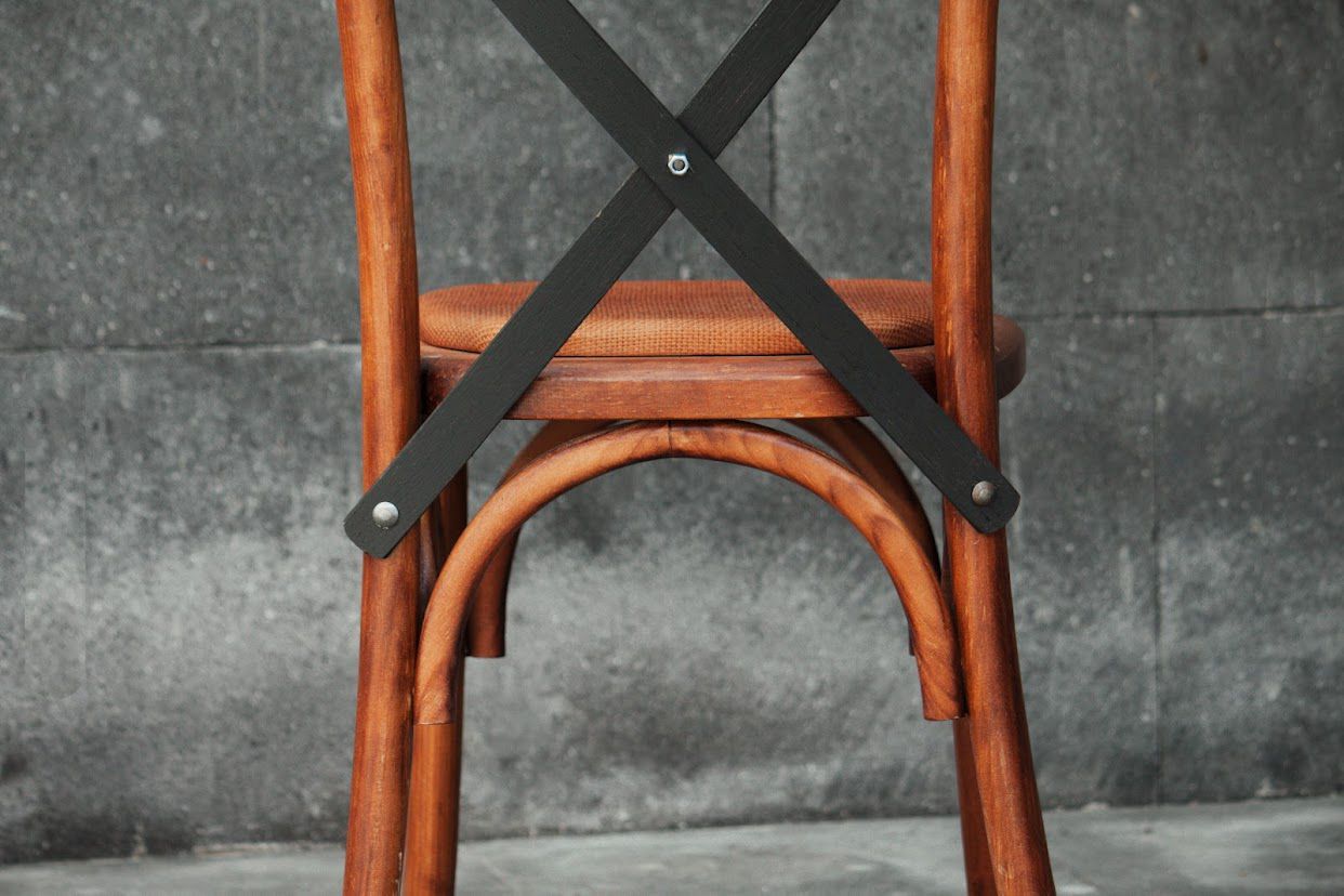 Respaldo de silla de madera con refuerzos en X de metal negro sobre un fondo gris moteado.