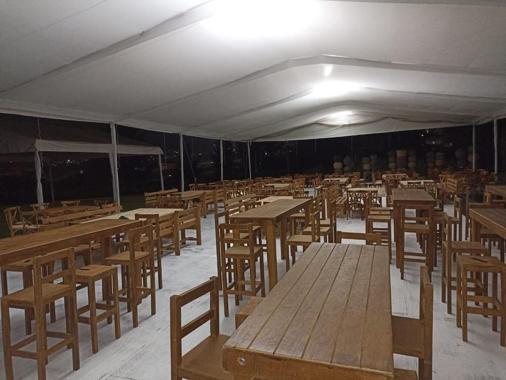 Mesas y sillas de madera instaladas bajo una carpa blanca para un evento.