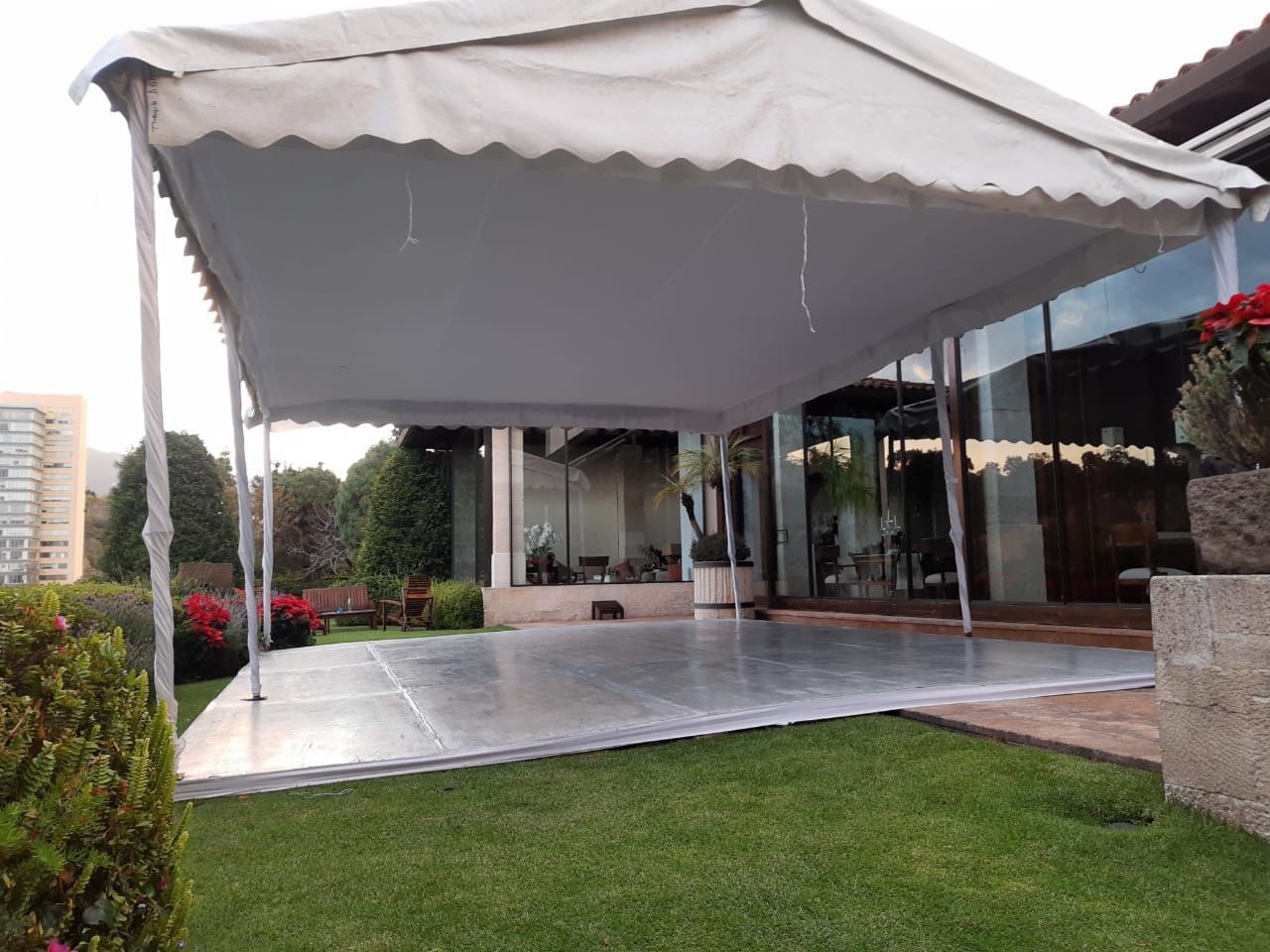 Carpa blanca sobre una pista de baile sobre césped verde, con una casa al fondo.
