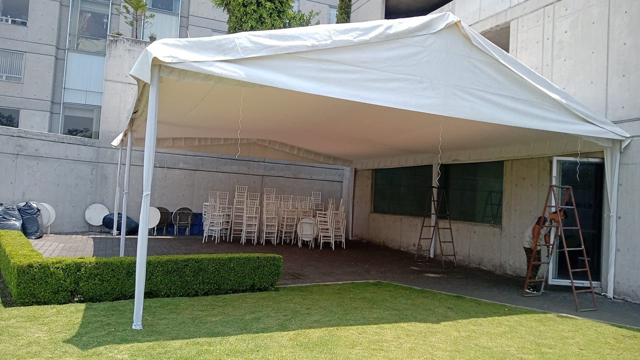 Carpa blanca instalada al lado de un edificio sobre césped con sillas en el interior.