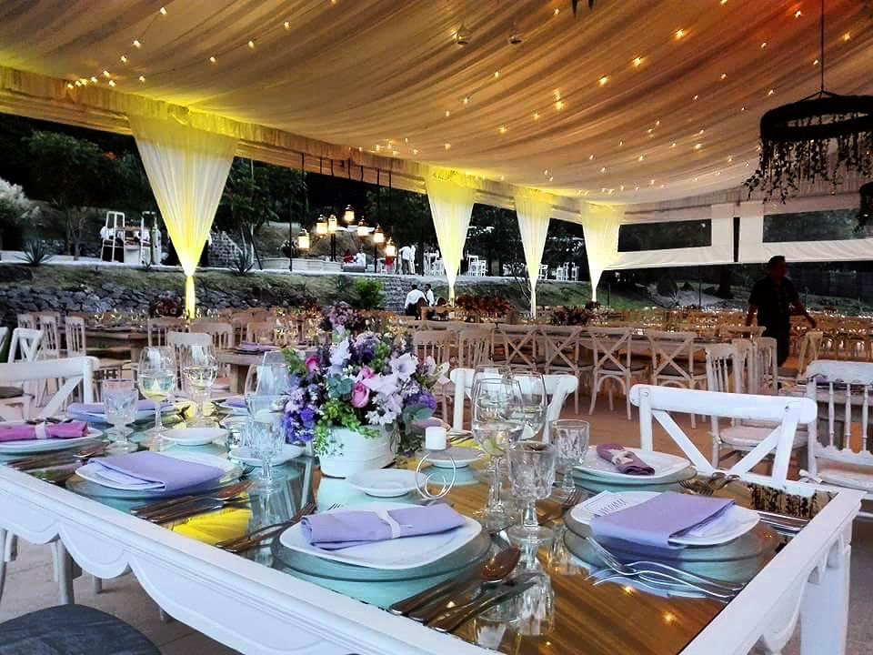 Recepción de boda con mesas preparadas para los invitados, techo cubierto y centros de mesa florales.