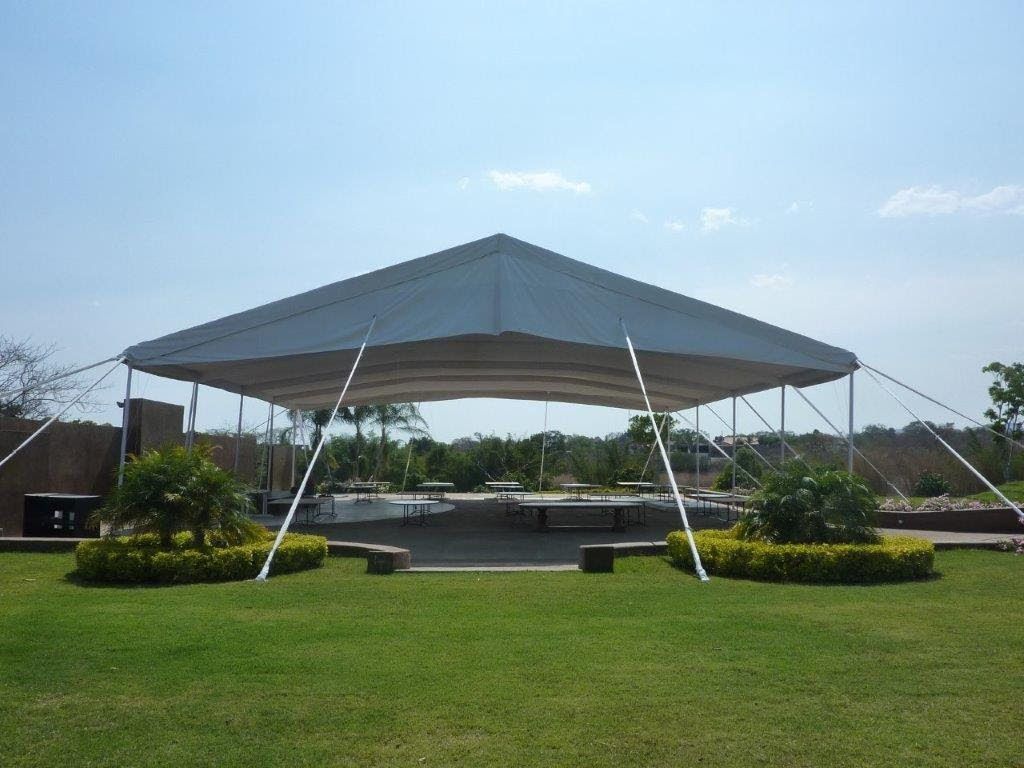 Carpa blanca sobre un patio con asientos, sobre un césped bajo un cielo azul claro.