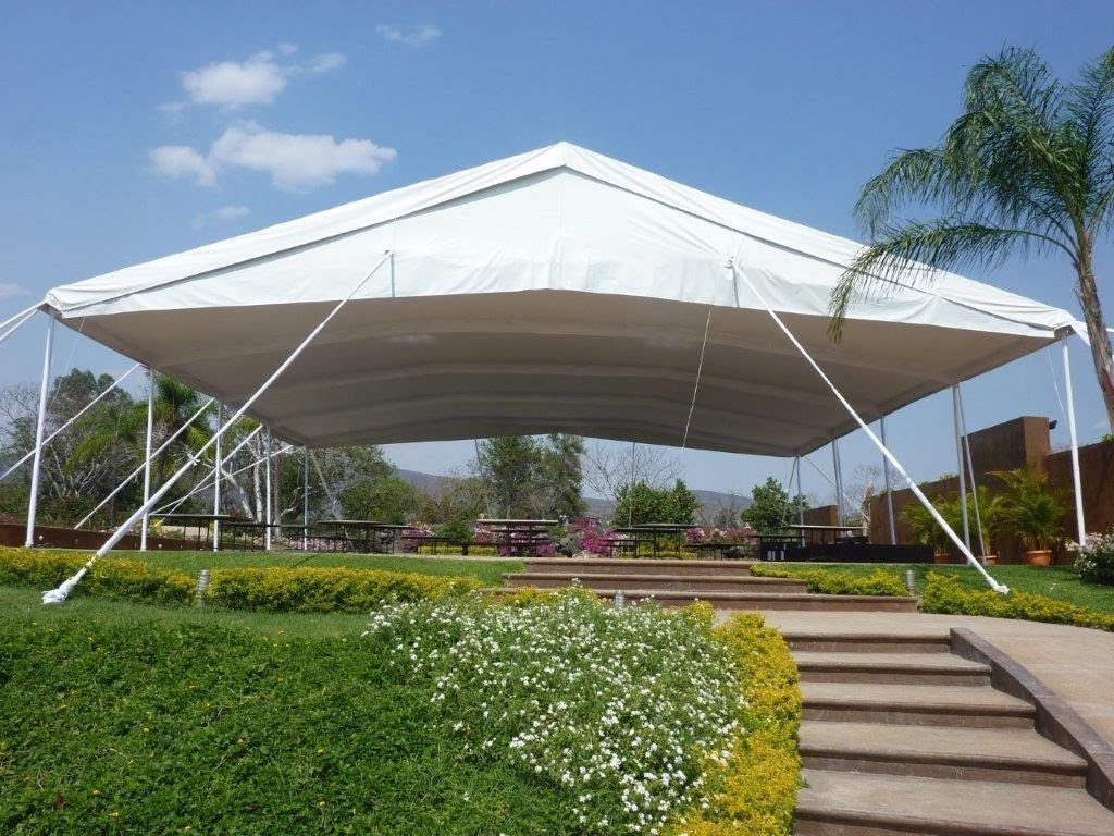 Estructura de carpa blanca sobre un área preparada con asientos y jardinería; al aire libre en un día soleado.