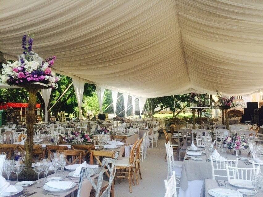 Recepción de boda bajo una carpa blanca, mesas preparadas con flores y cubiertos.