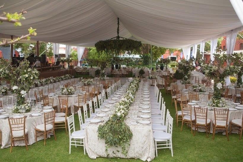 Recepción de boda al aire libre con mesas largas, mantelería blanca, centros de mesa florales y una carpa cubierta.
