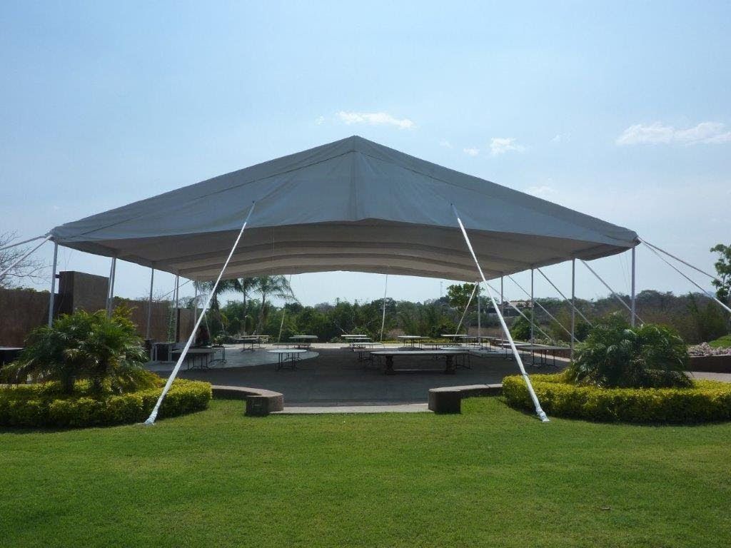 Gran carpa blanca instalada al aire libre, sobre mesas de picnic, en un día soleado.