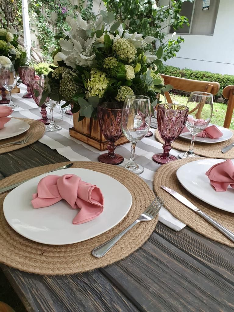 Decoración de mesa con servilletas rosas, copas de vino moradas y centro de mesa floral.