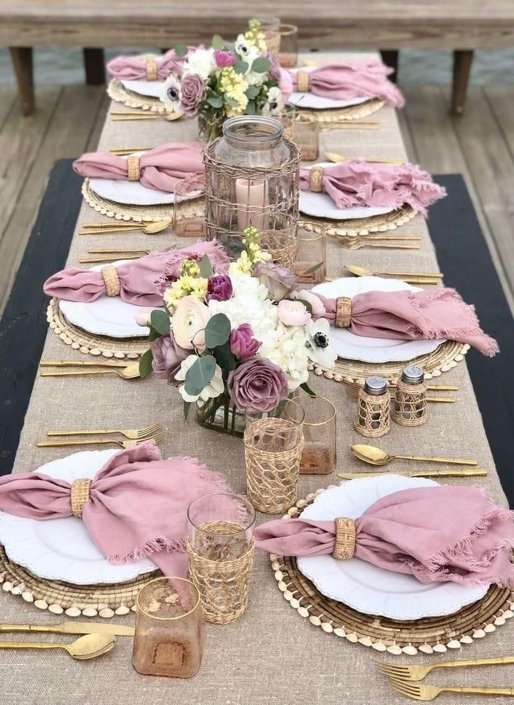 Elegante mesa con servilletas rosas, cubiertos dorados y centros de mesa florales.