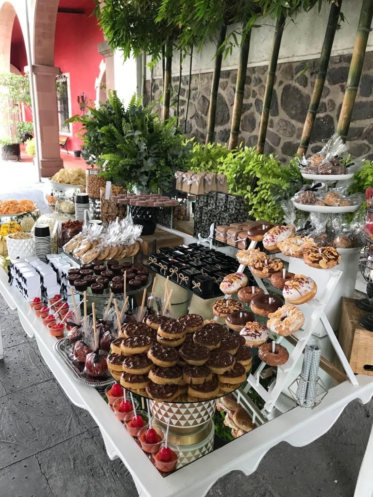 Bufé de postres en una mesa con muchas delicias, entre ellas donas, manzanas cubiertas de chocolate y pequeños pasteles.