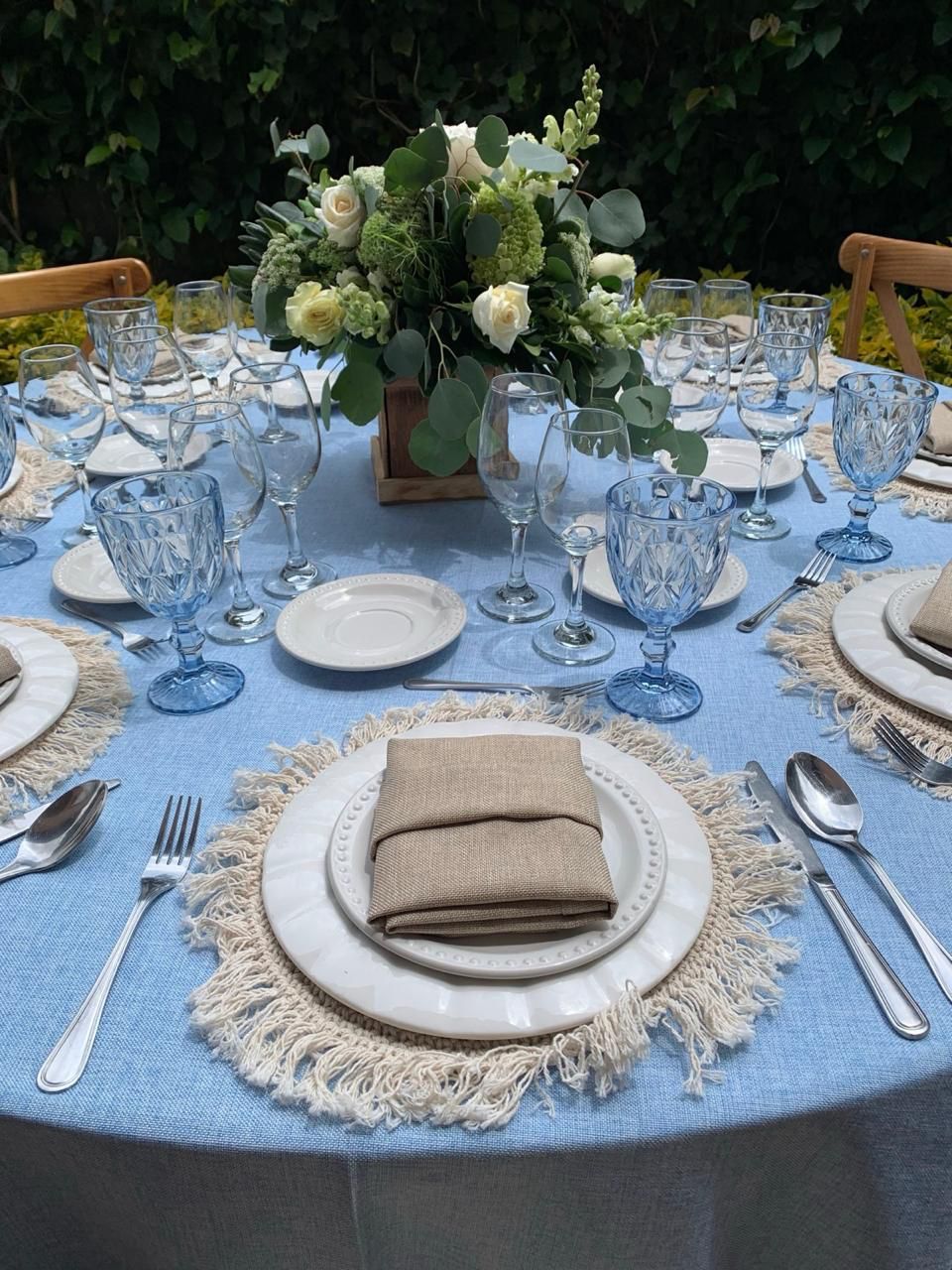 Mesa formal con mantel azul, centro de mesa floral y cristalería azul.