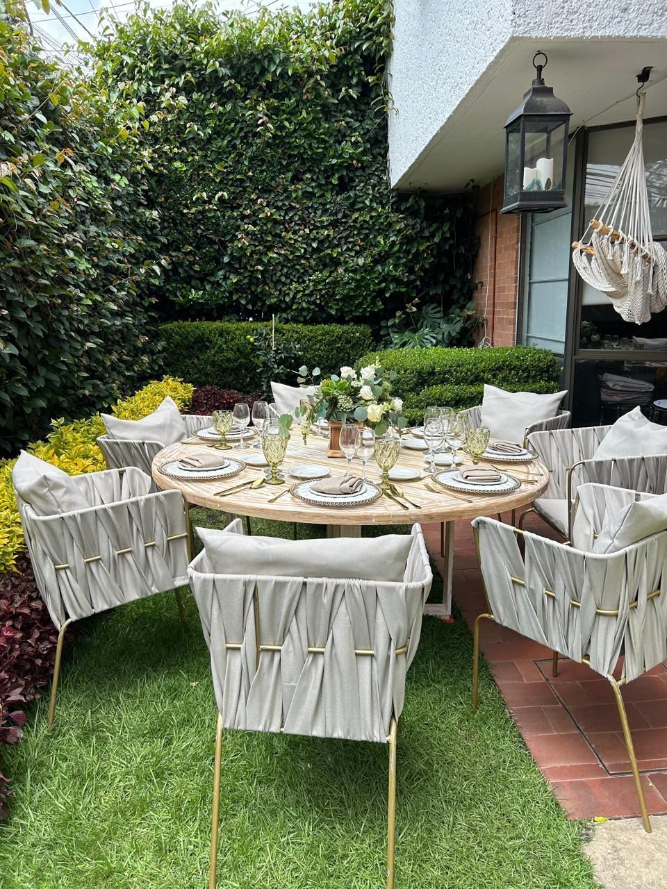Juego de mesa de comedor al aire libre para invitados, rodeado de follaje verde, patio y sillas.
