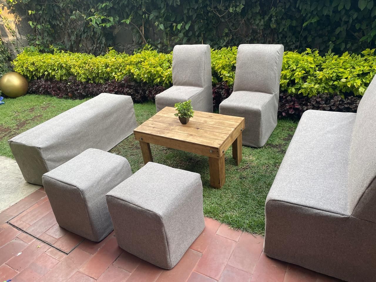 Zona de estar al aire libre con muebles tapizados en tela beige y una mesa de madera sobre un césped verde.