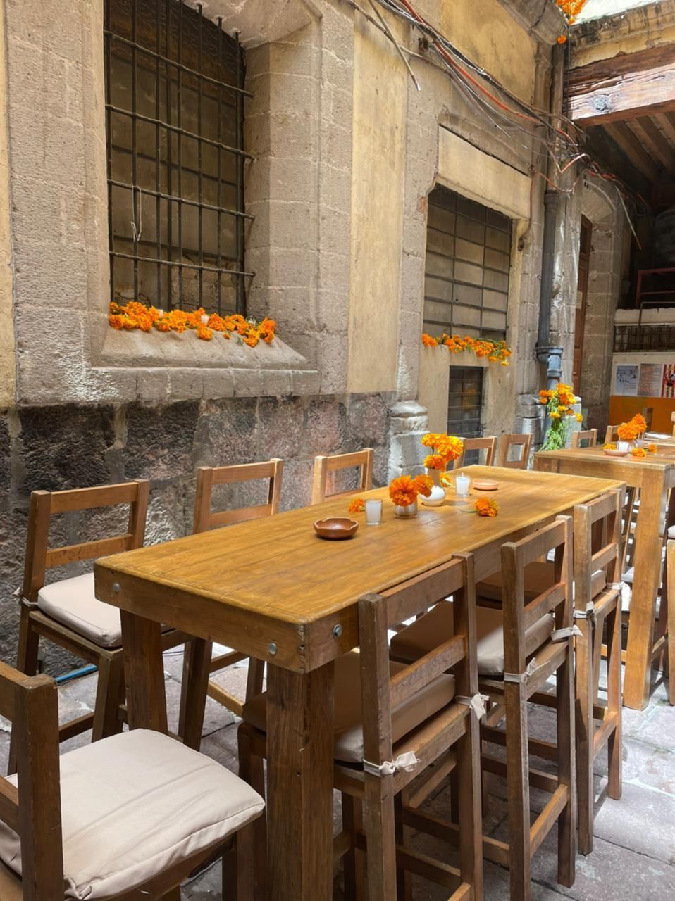Restaurante al aire libre con mesas y sillas de madera, decorado con flores de color naranja y velas.