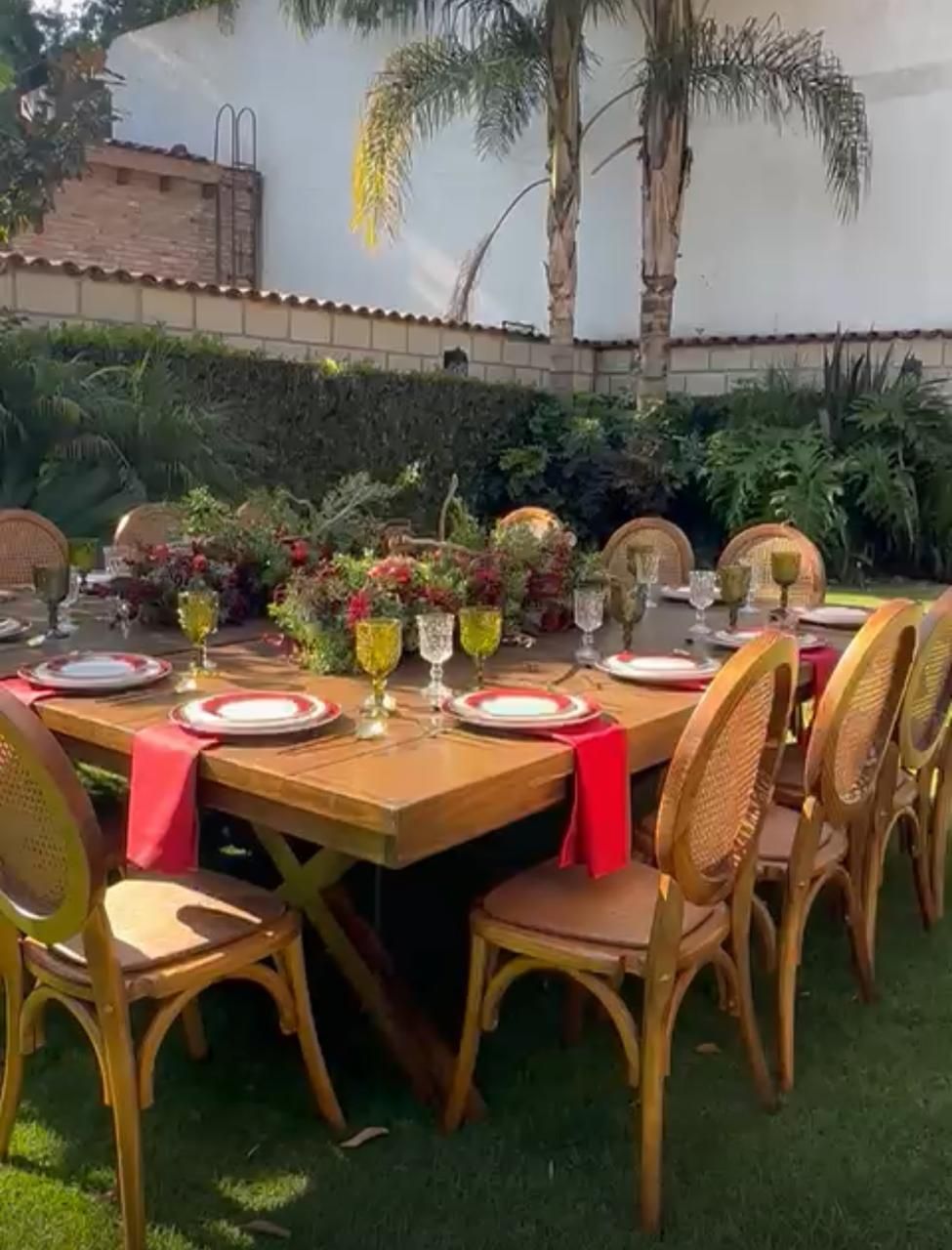 Mesa de comedor al aire libre para comer. Mesa de madera marrón, servilletas rojas y sillas de ratán. Fondo de vegetación.