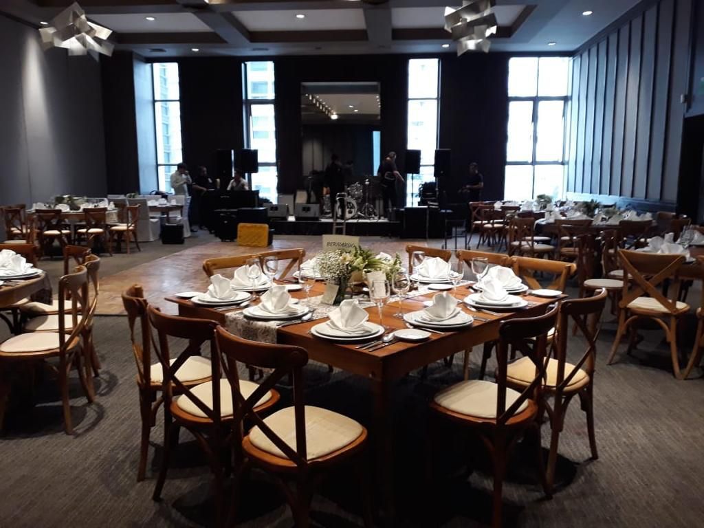 Comedor formal preparado para evento con mesas cuadradas, sillas y una banda en un escenario de fondo.