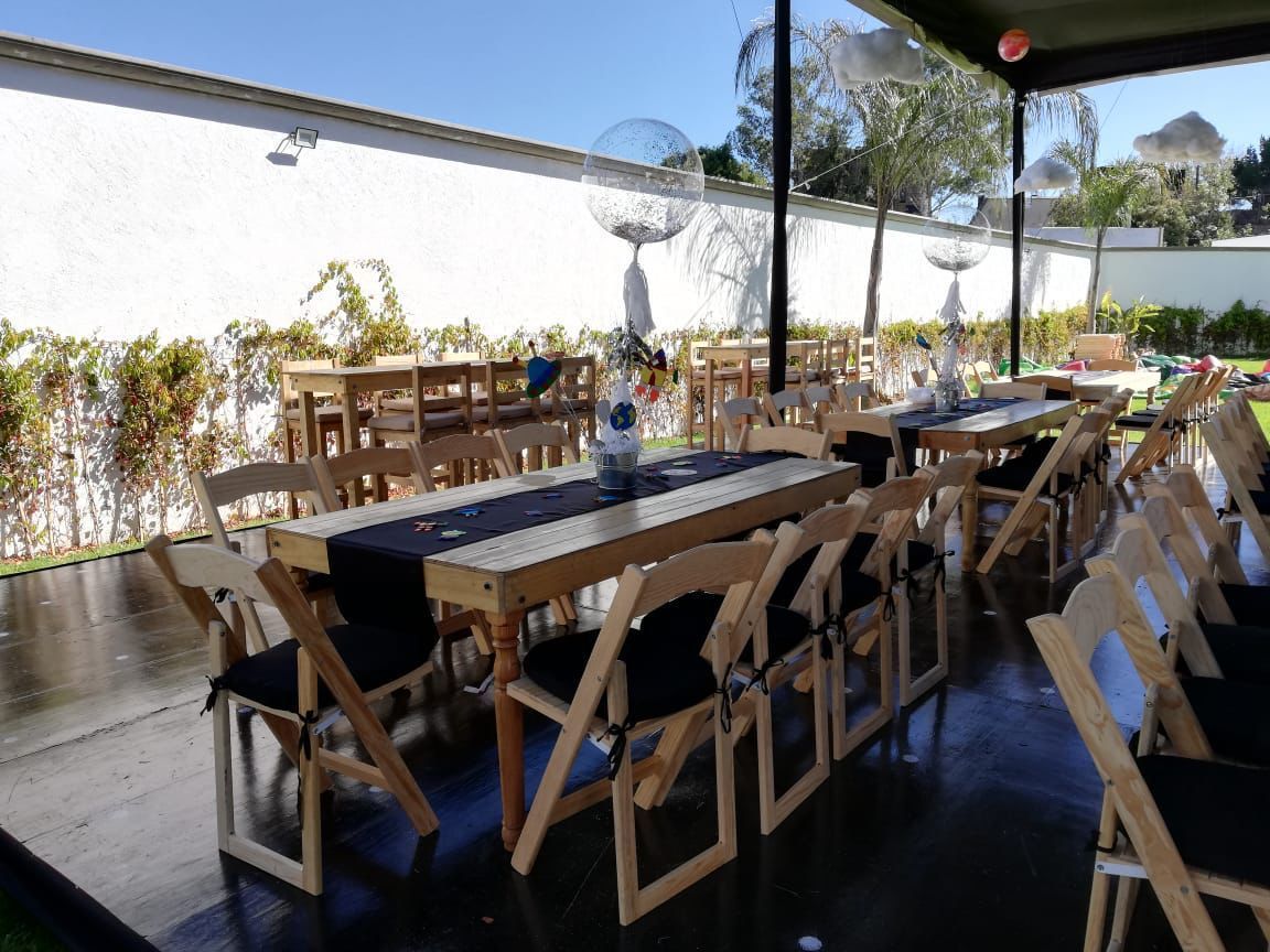 Mesas para eventos al aire libre con sillas instaladas bajo un área cubierta y a lo largo de una pared blanca.