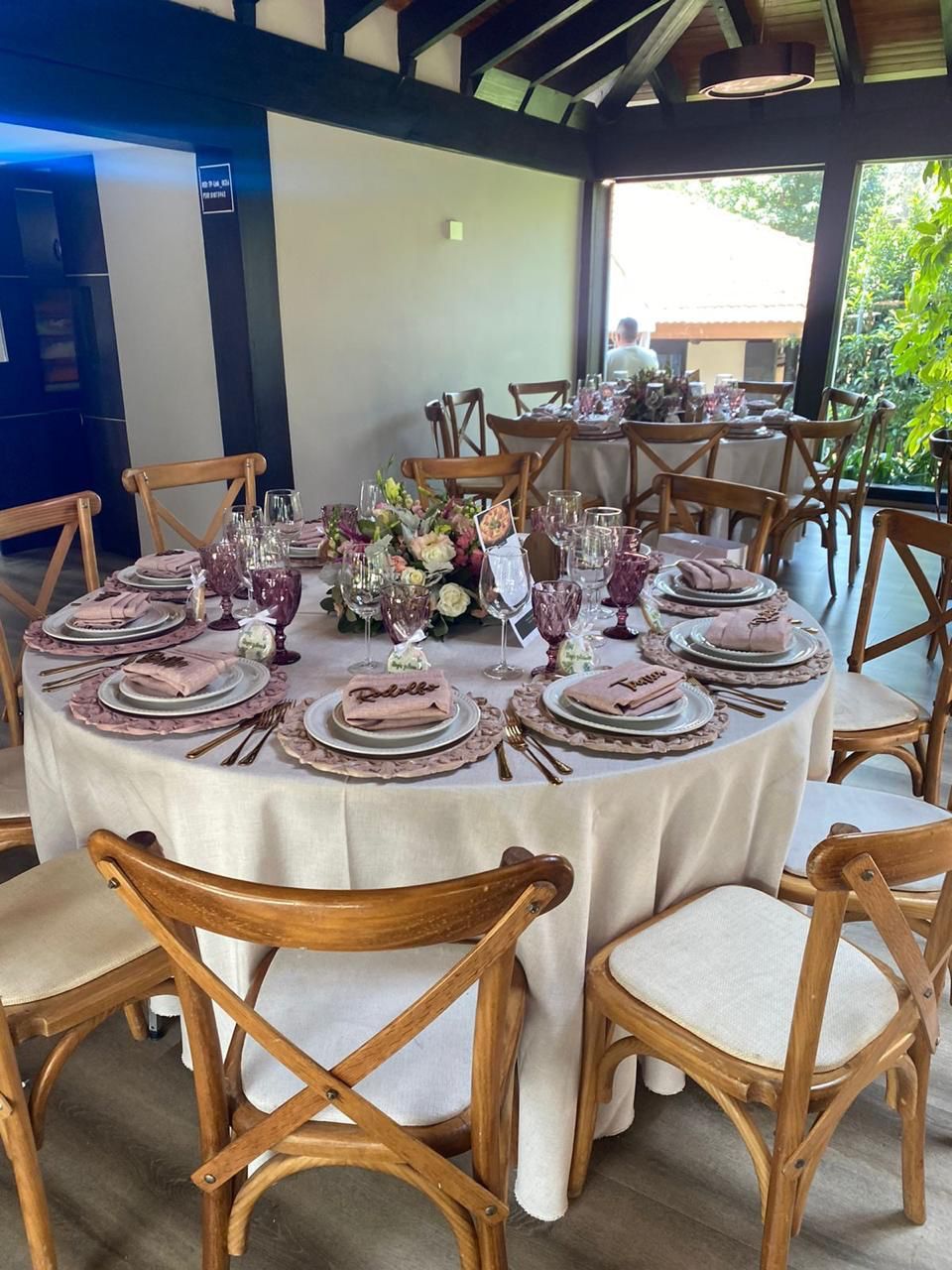 Mesa redonda para evento formal con centros de mesa florales, cristalería morada y sillas de madera.