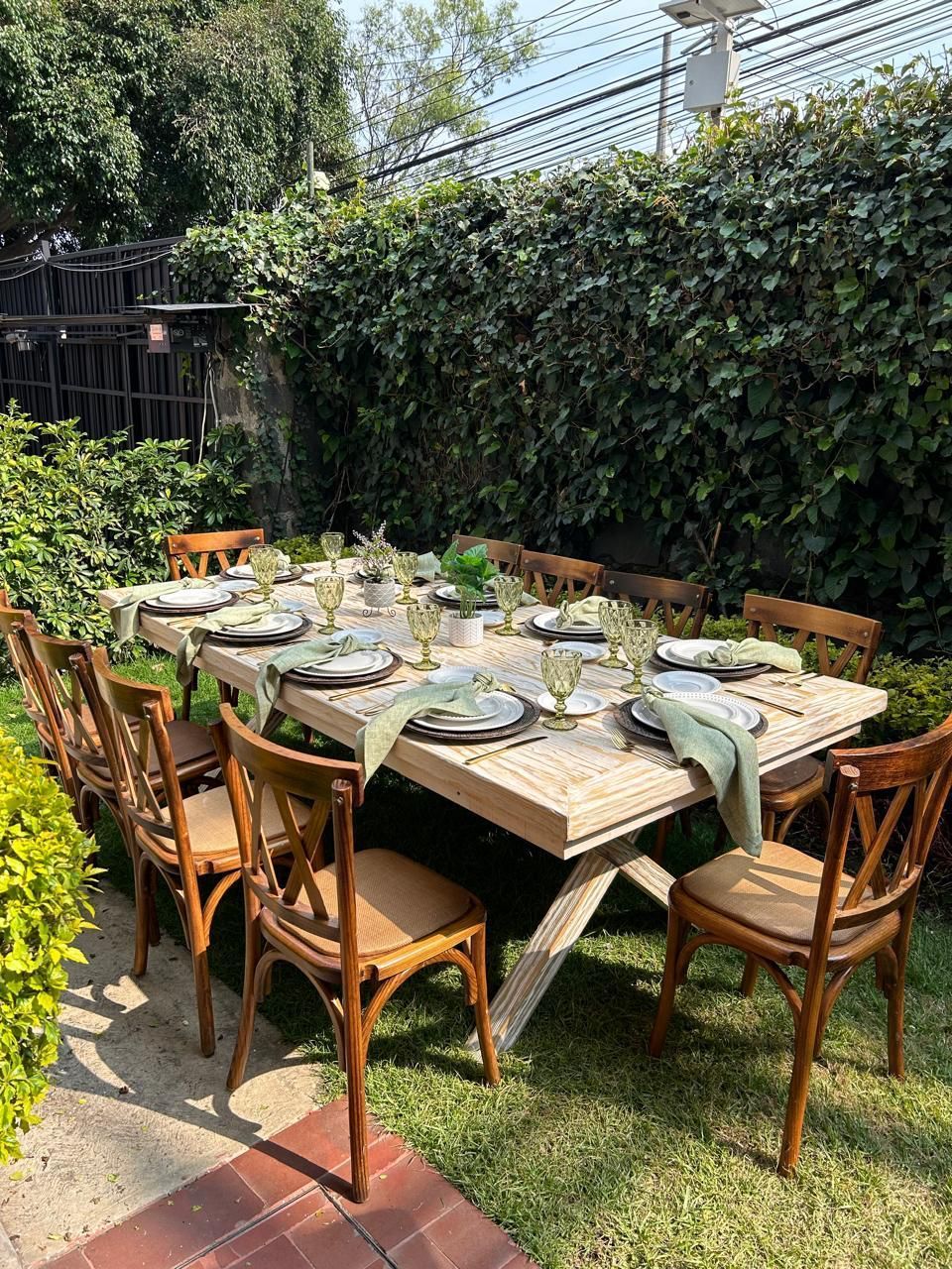 Mesa de comedor al aire libre para una reunión, rodeada de sillas en un césped verde con una exuberante pared verde.