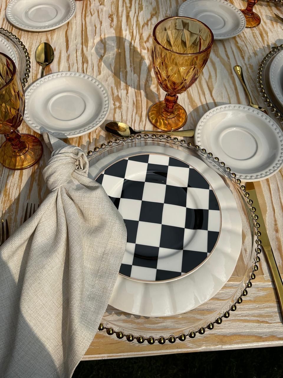 Puesta de mesa con plato cuadriculado, copa color ámbar y cubiertos dorados.