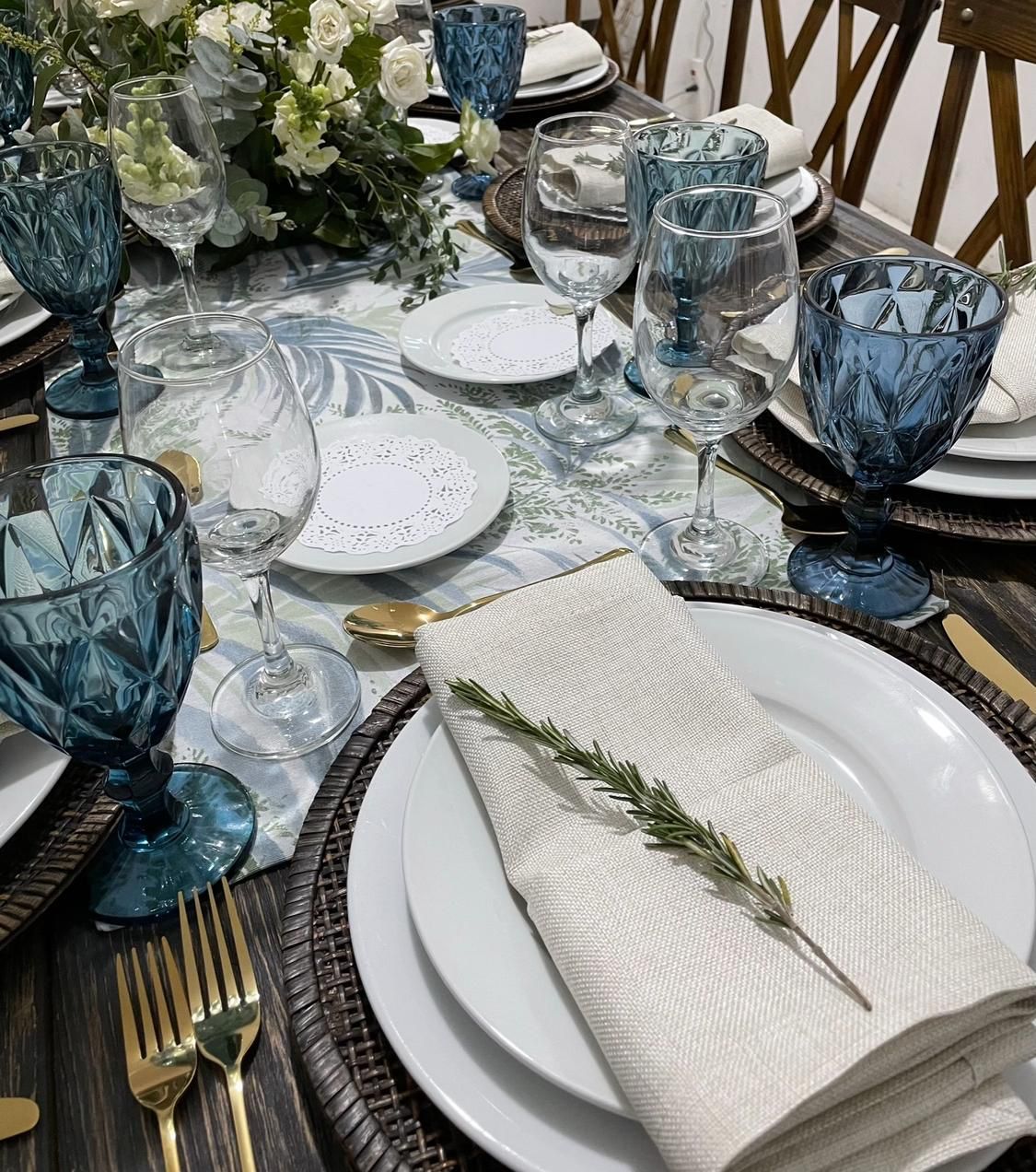 Elegante mesa con cristalería color verde azulado, platos blancos y cubiertos dorados.