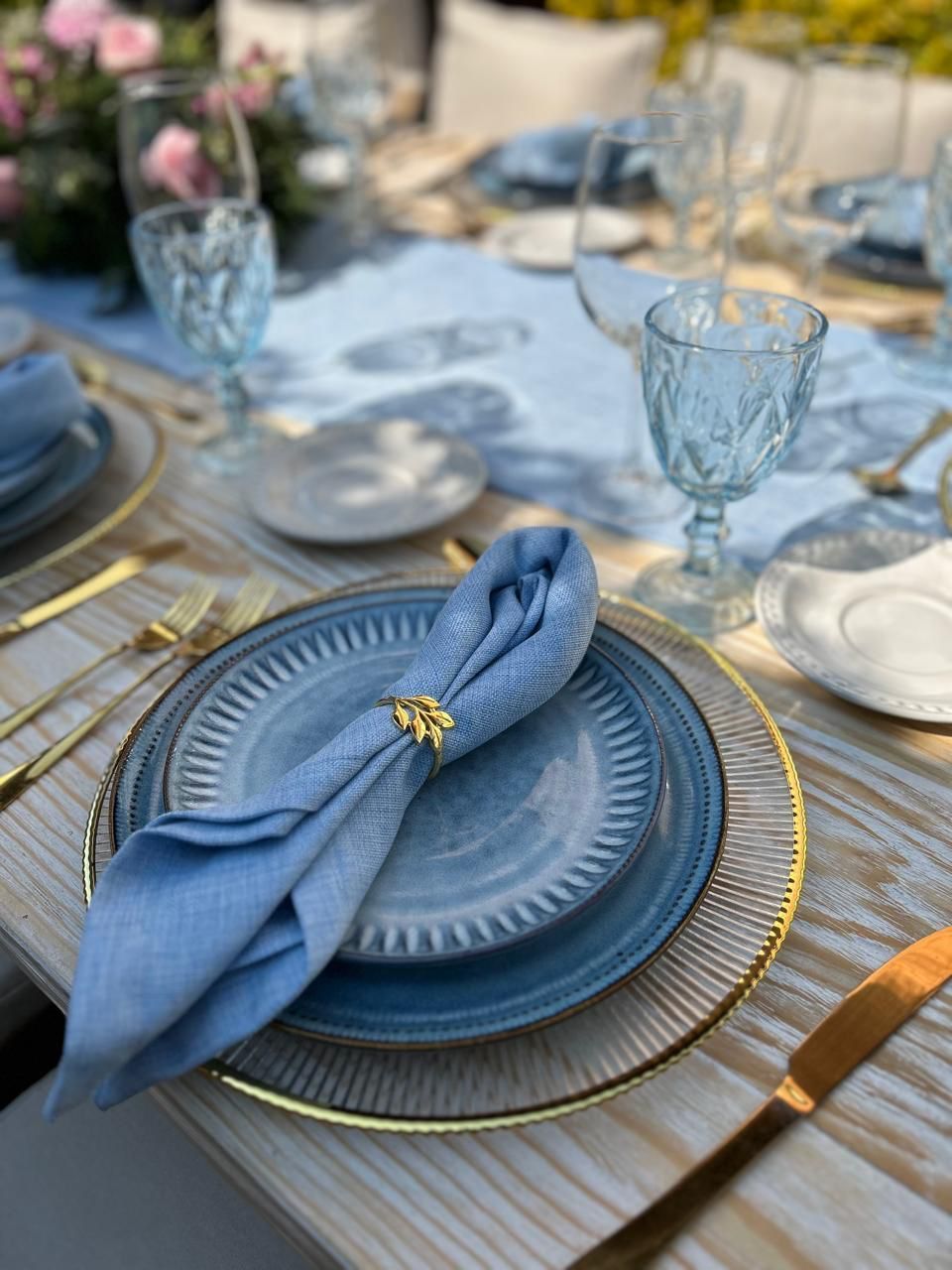 Elegante mesa con platos azules, cubiertos dorados y servilletero.
