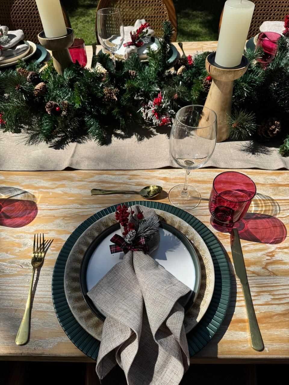 Mesa festiva con guirnalda navideña, cubiertos dorados y cristalería roja.