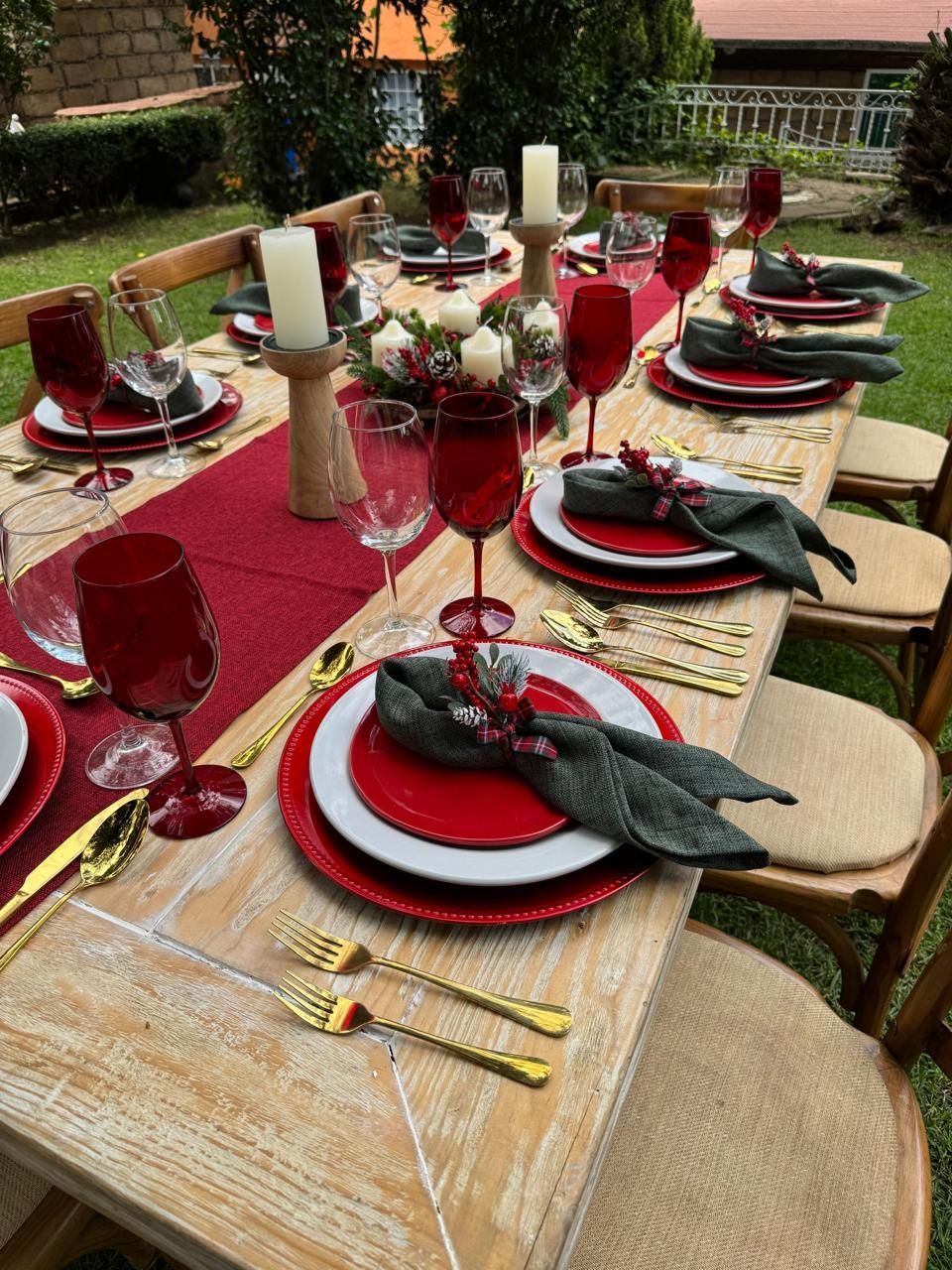 Juego de mesa de comedor al aire libre para una ocasión formal con decoración en rojo y dorado, incluye vasos y cubiertos.