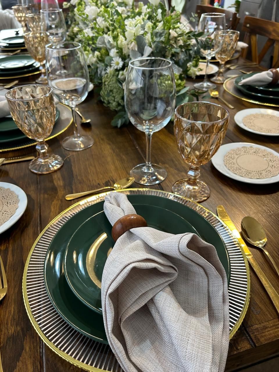 Mesa de comedor formal con platos verdes, detalles dorados y un centro de mesa floral.