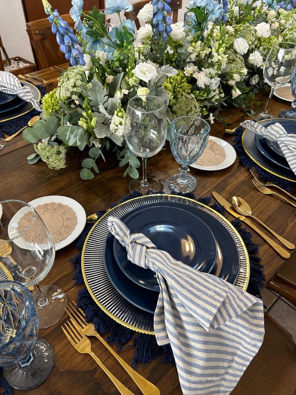 Elegante mesa con detalles en azul y dorado, con centro de mesa y cubiertos florales.
