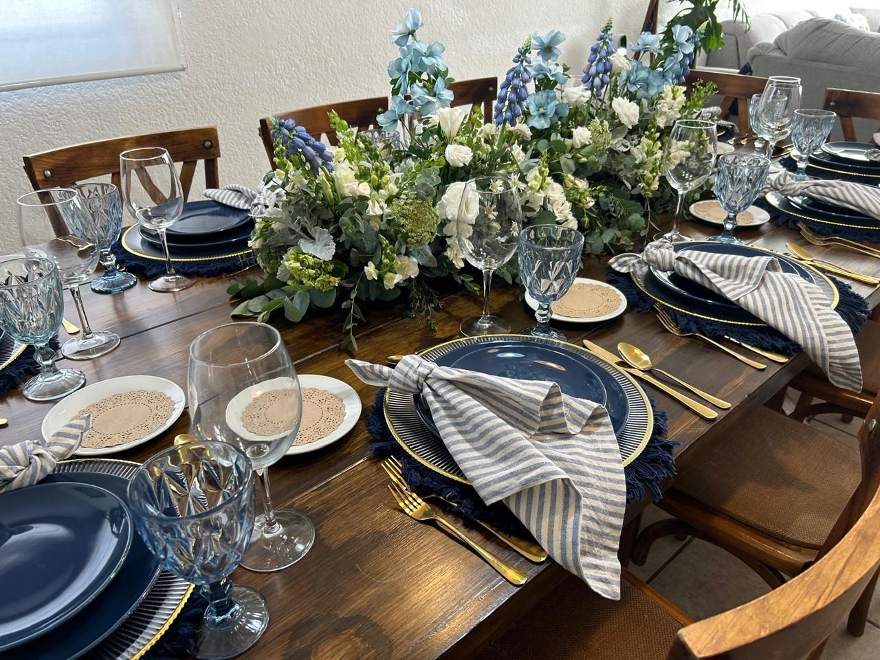 Juego de mesa de comedor formal con platos azules y dorados, servilletas a rayas y un centro de mesa floral.