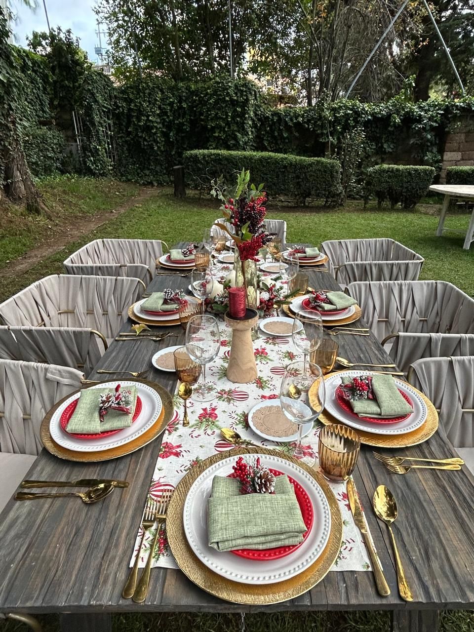 Mesa navideña al aire libre con detalles dorados, manteles individuales rojos y verdes y centro de mesa floral.