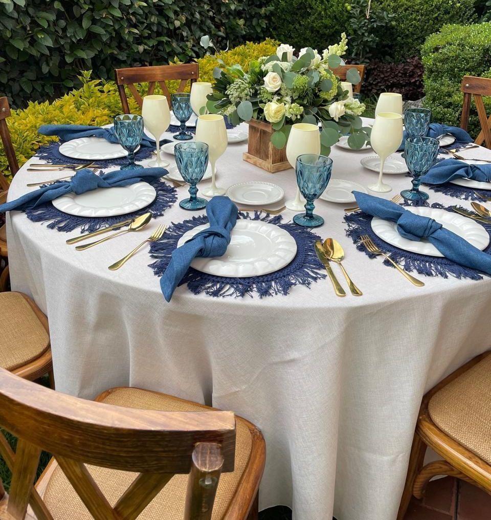 Conjunto de mesa redonda para cenar al aire libre con detalles en azul y dorado, mantel blanco.